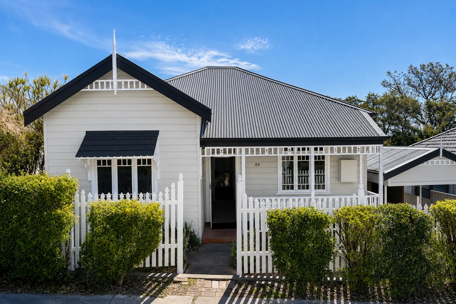 White cottage facade with a dark roof and white picket fence.