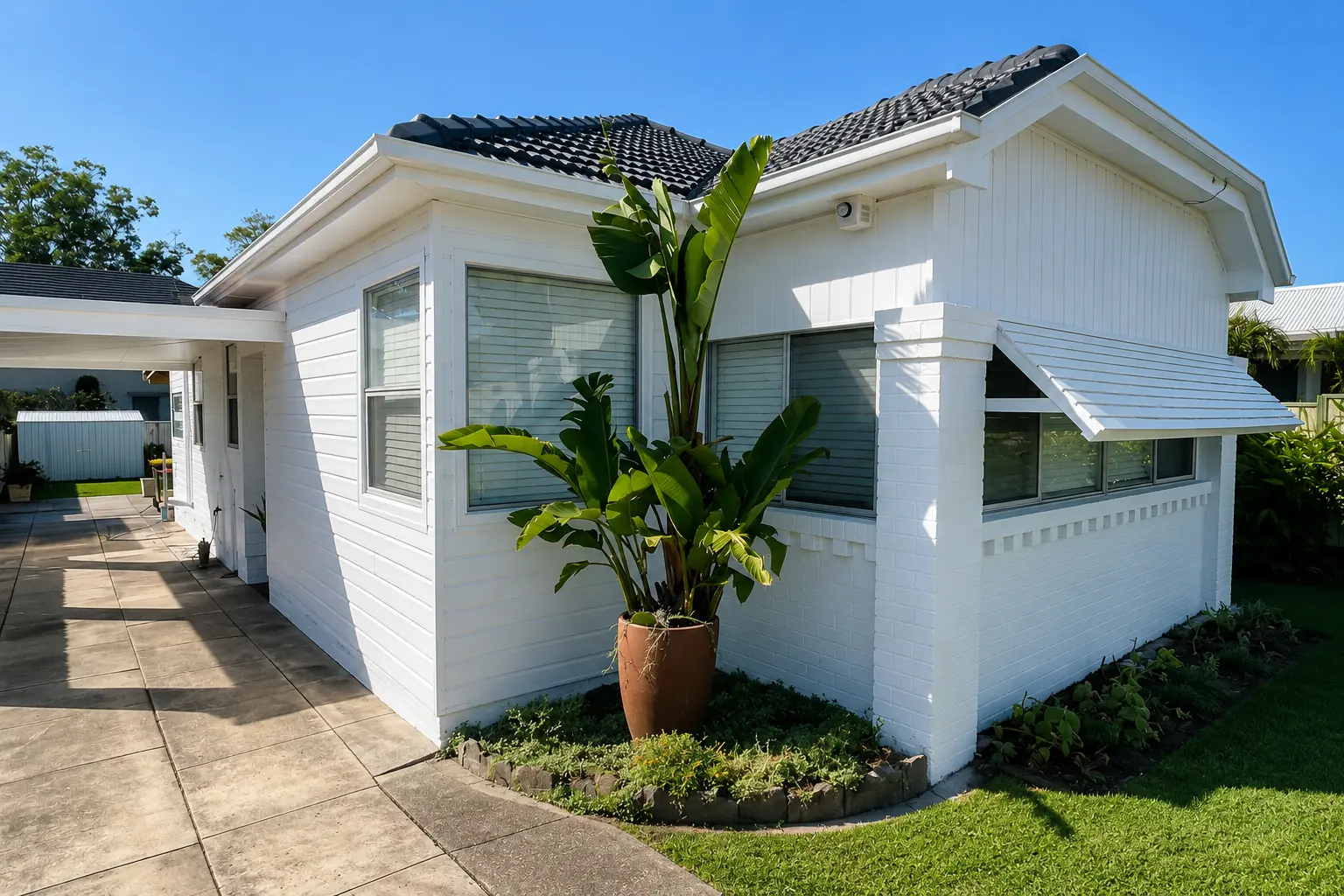 White house exterior with covered veranda, posts and surrounding garden.