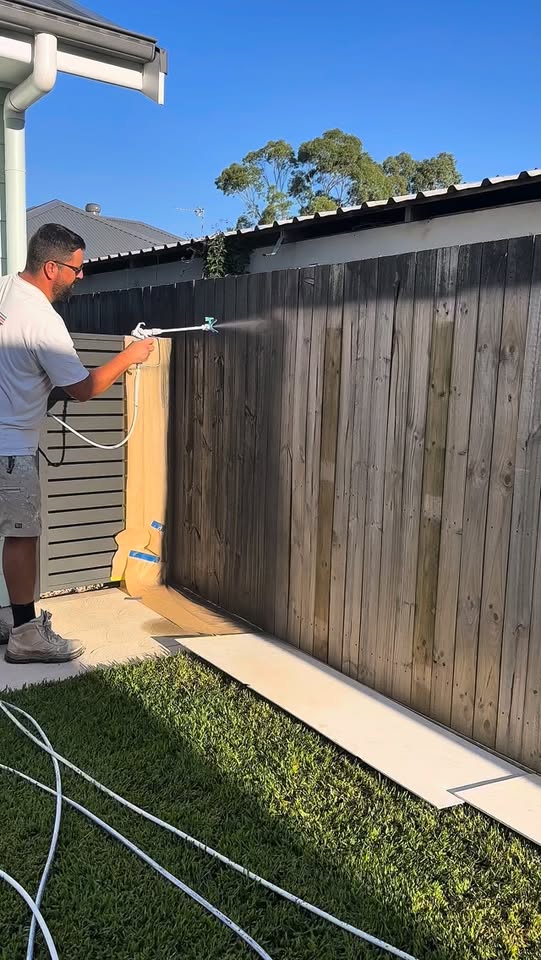 AdvaPaint spraying a timber fence black, with adjacent surfaces masked.