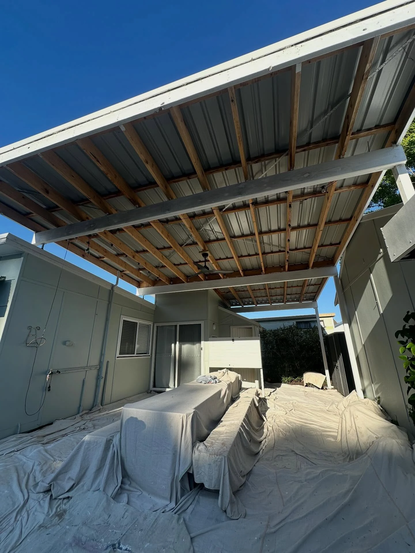 Drop cloths protect an outdoor patio beneath unpainted roof framing.