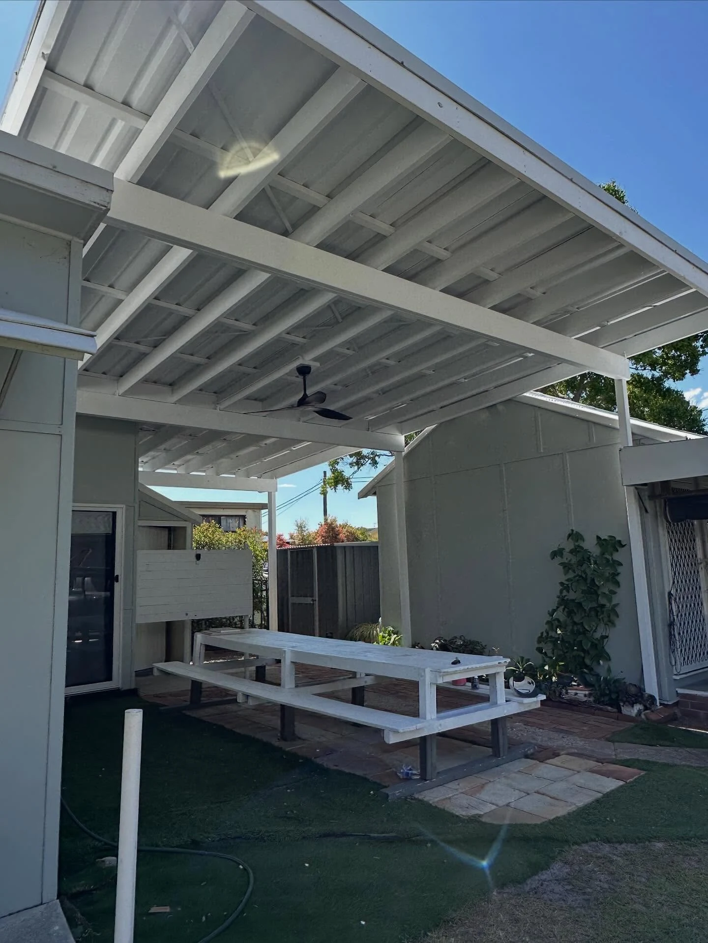 Outdoor patio with painted white roof framing and posts above an outdoor table.